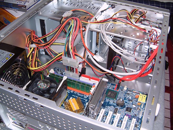 [写真：HDD・DVD・FDDなどをマザーボードとPCケースに取り付ける作業。配線がごちゃごちゃしています。]